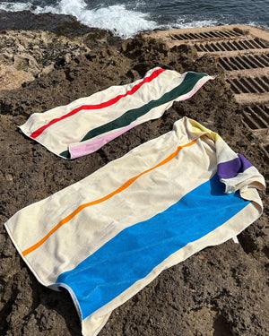 Two beach towels with colorful stripes on a sandy surface near water.